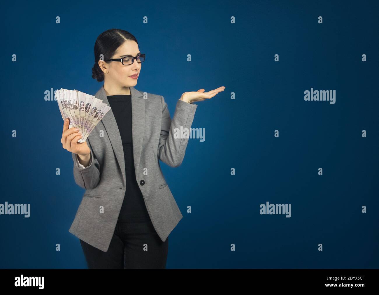 Belle jeune femme en lunettes tient beaucoup de ruble russe billets dans sa main avec l'espace de copie. Banque D'Images