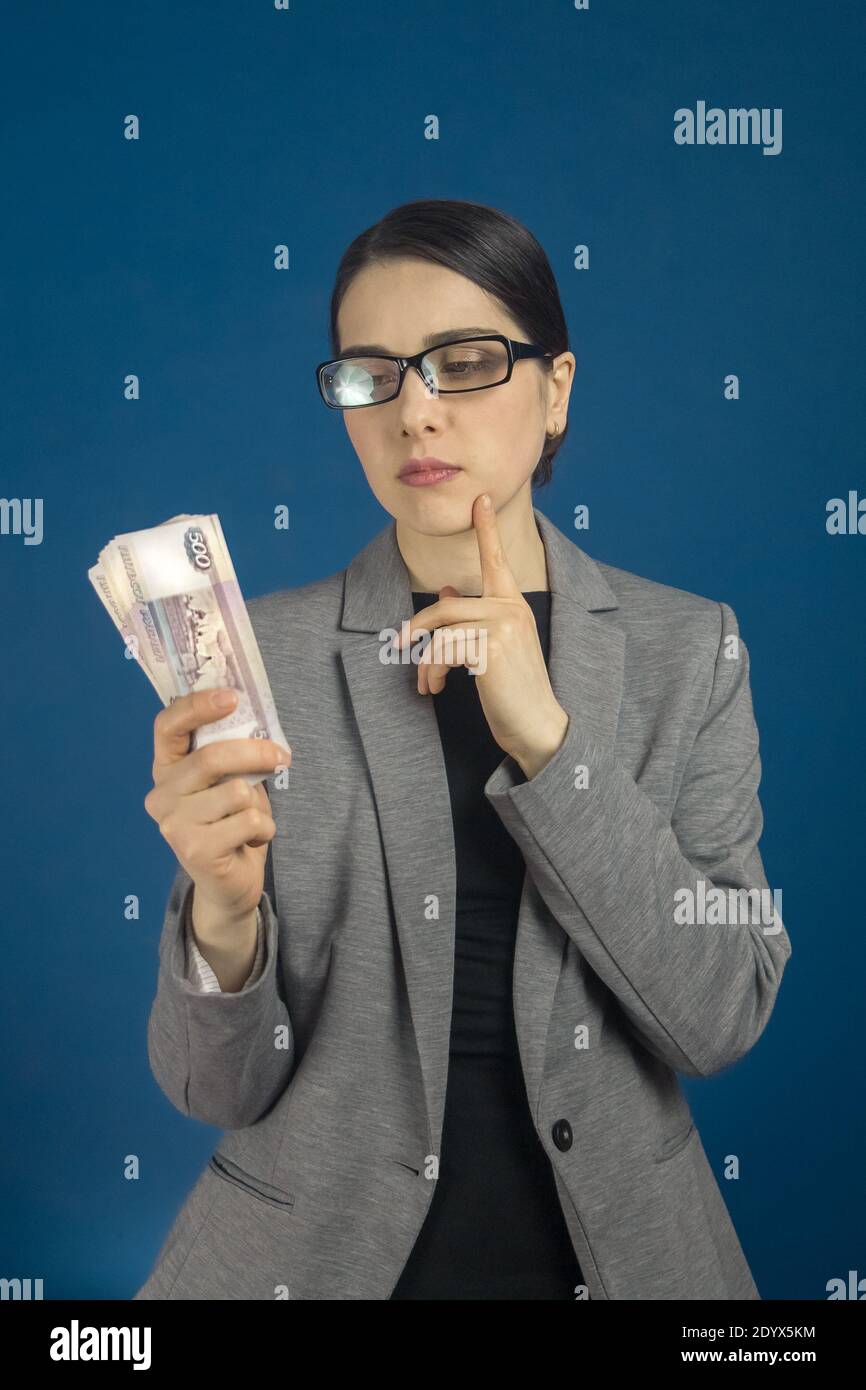 Une jeune femme en lunettes regarde un paquet de rouble russe avec intérêt sur fond bleu. Mise au point verticale sélective. Banque D'Images