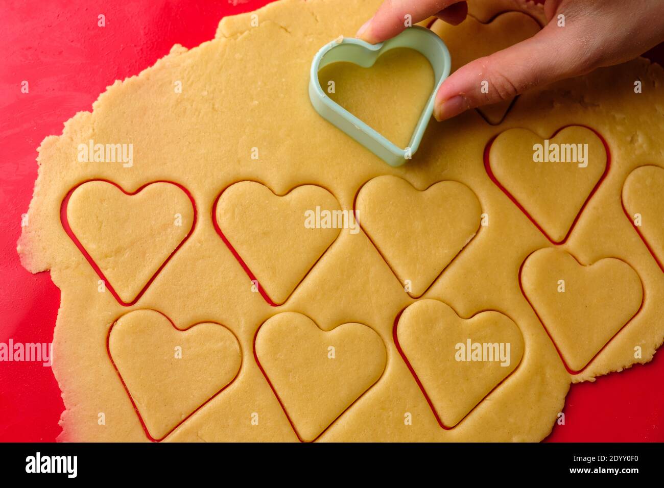 Faire des biscuits de pain d'épice en forme de coeur à l'aide d'un couteau en plastique sur le tapis de cuisson en silicone rouge. Bonbons pour la Saint-Valentin. Banque D'Images