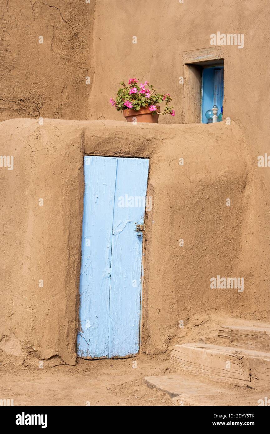 Gros plan d'une maison en adobe avec porte peinte en bleu et un pot de géraniums. Le village historique d'adobe amérindien de Taos Pueblo, Nouveau-Mexique Banque D'Images
