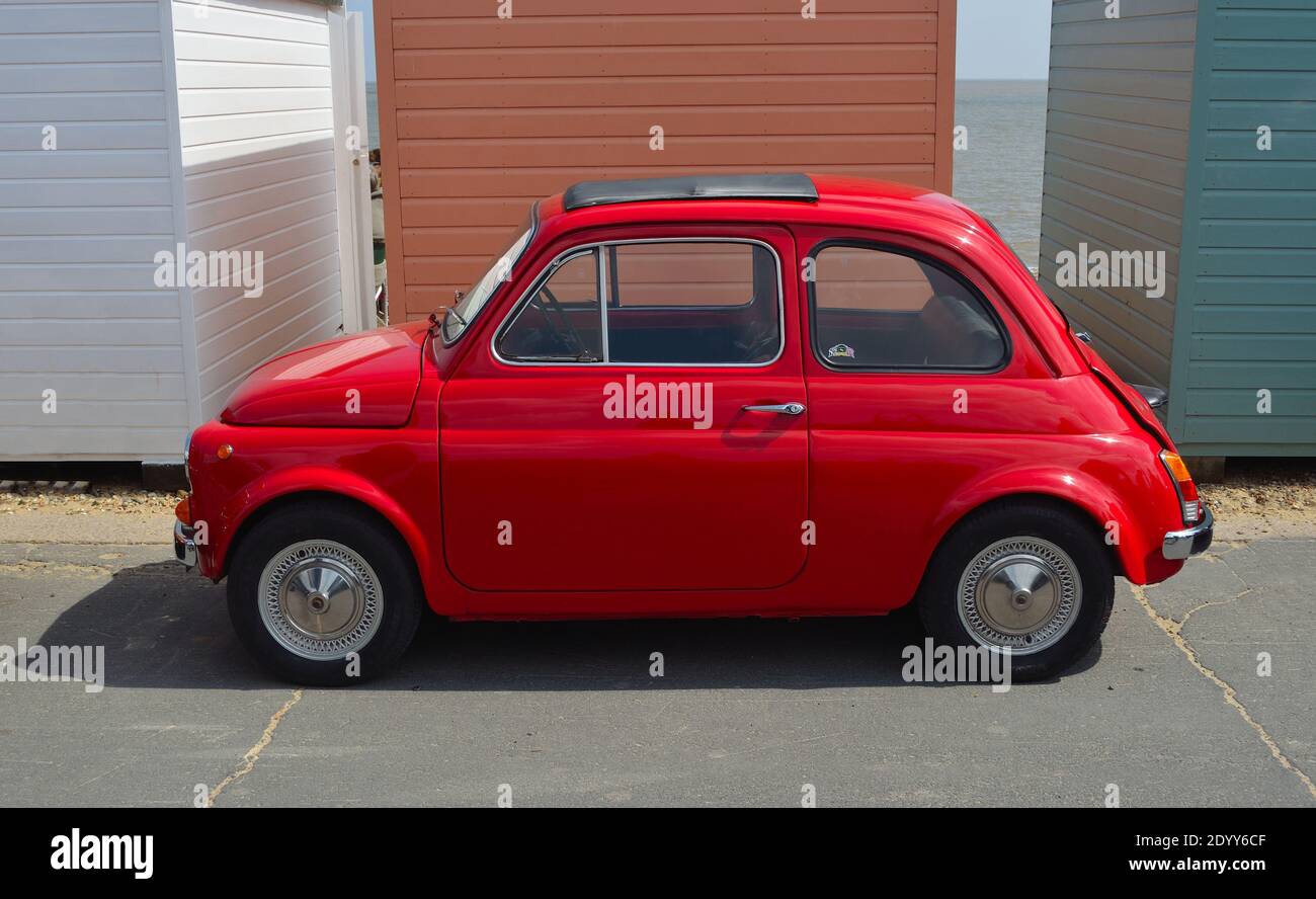 Voiture classique Rouge Fiat 500 garée sur la promenade du front de mer en face des cabanes de plage. Banque D'Images