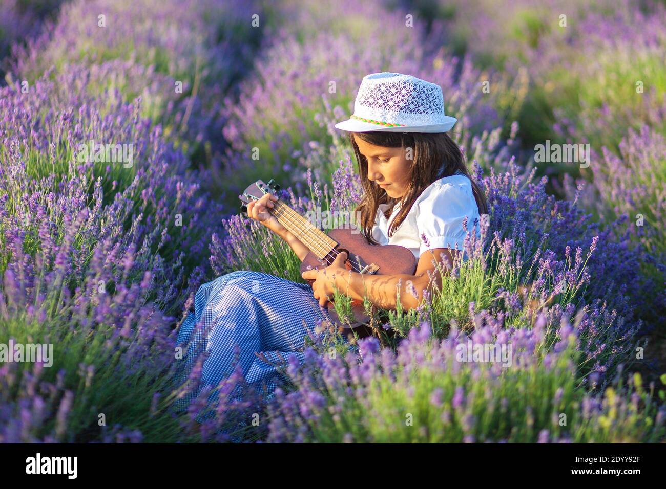 Belle fille de campagne dans un chapeau joue une petite guitare assis dans un champ de lavande Banque D'Images