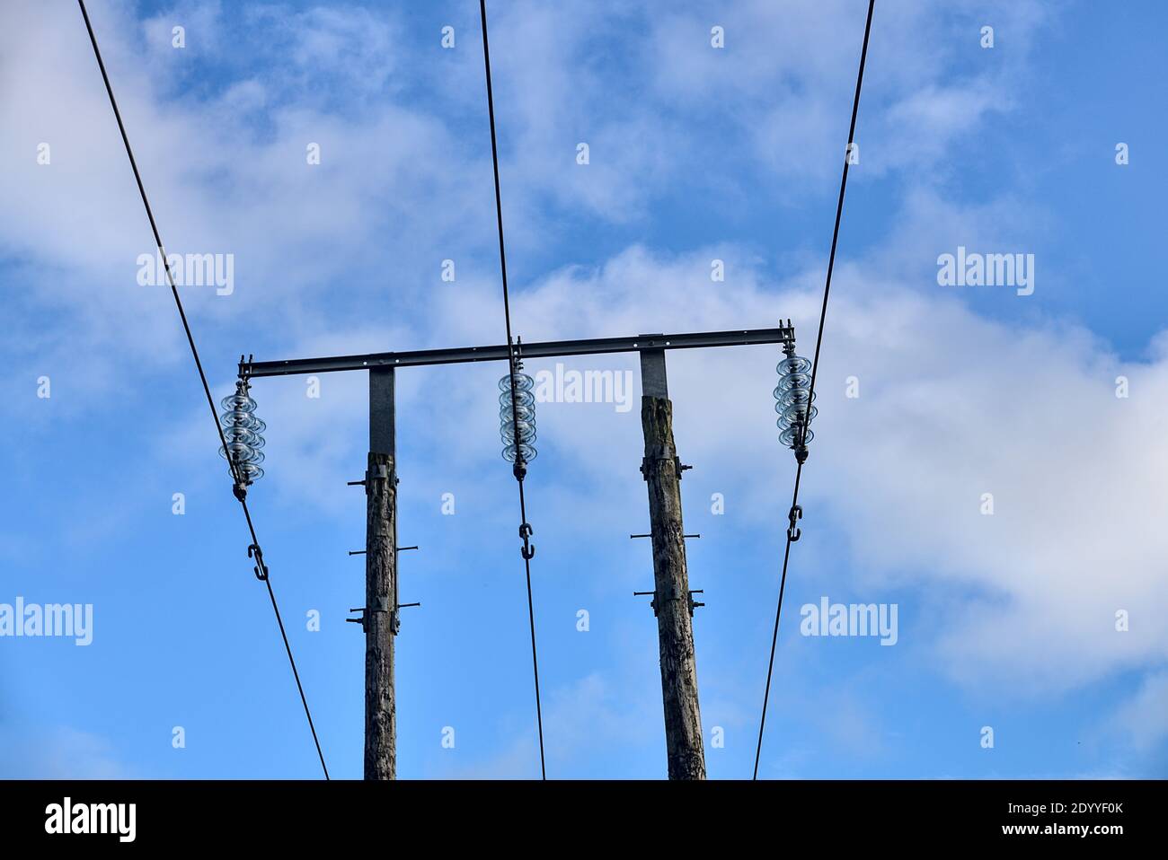 Lignes électriques aériennes sur un ancien pilier en bois capturé contre le ciel bleu avec des nuages blancs doux à Co. Dublin, Irlande. Trois fils de tension Banque D'Images