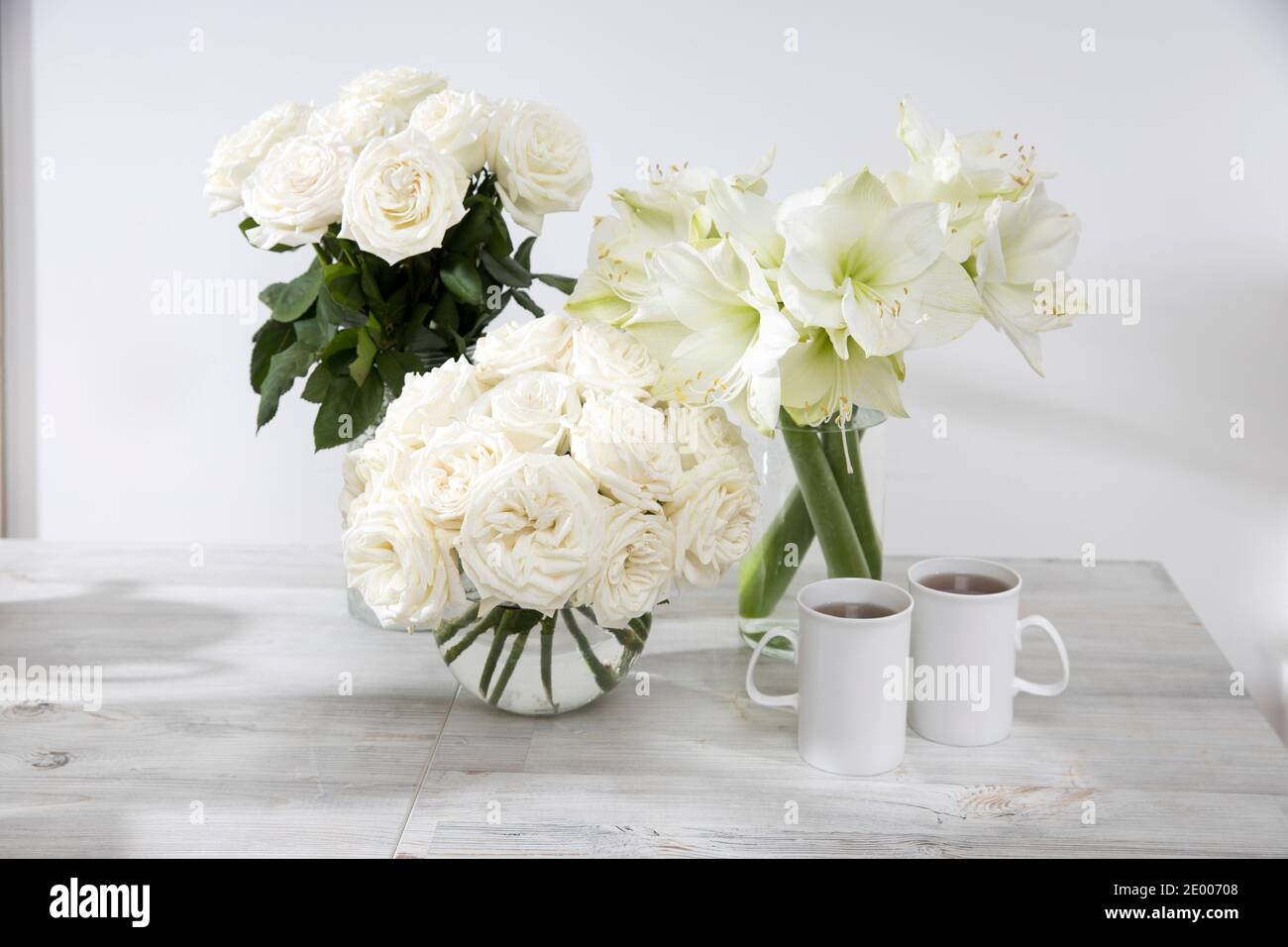 Roses blanches, nénuphars, dans des vases ronds avec deux tasses de café sur la table pour une occasion spéciale comme décoration de cuisine. Copier l'espace Banque D'Images