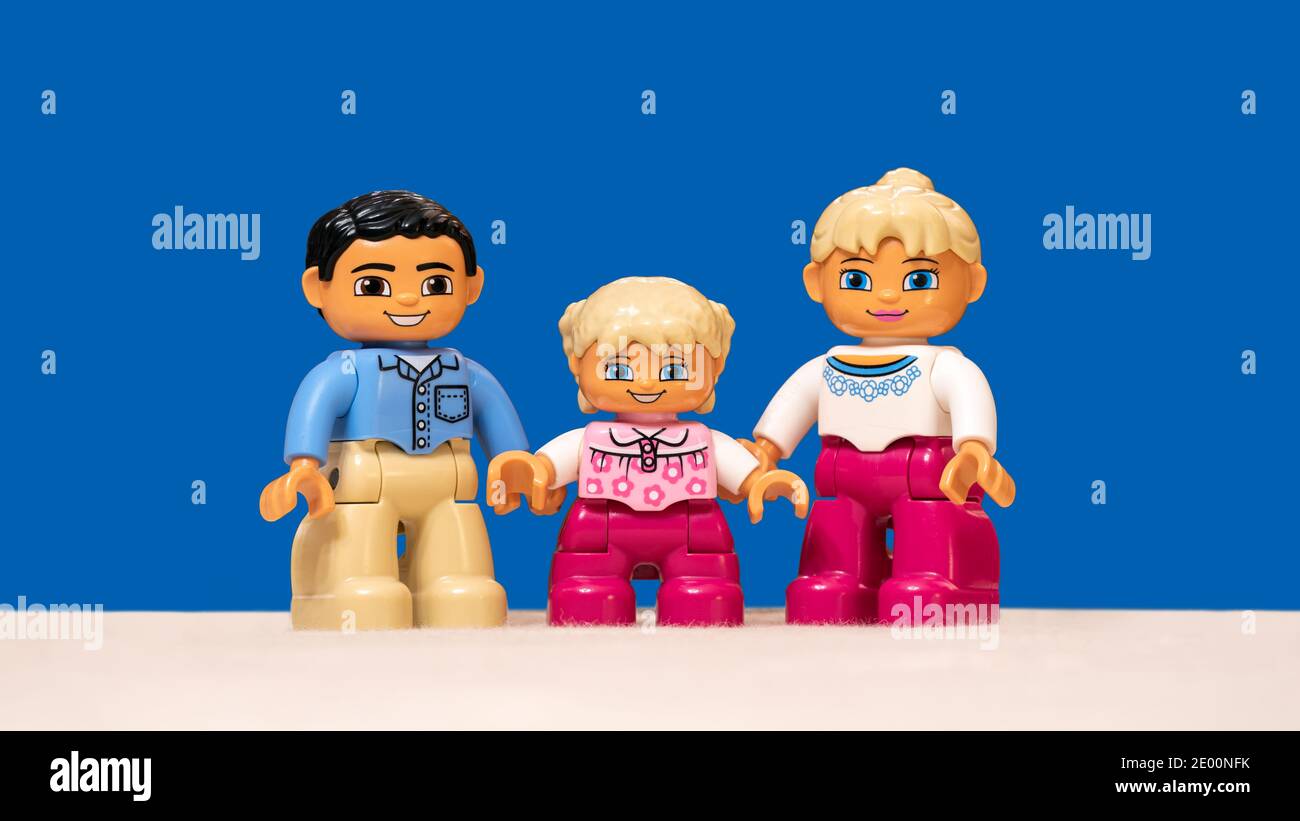 Emballage de trois figurines Lego représentant une famille modèle heureuse (papa, maman et fille souriant) isolée sur fond bleu. Banque D'Images
