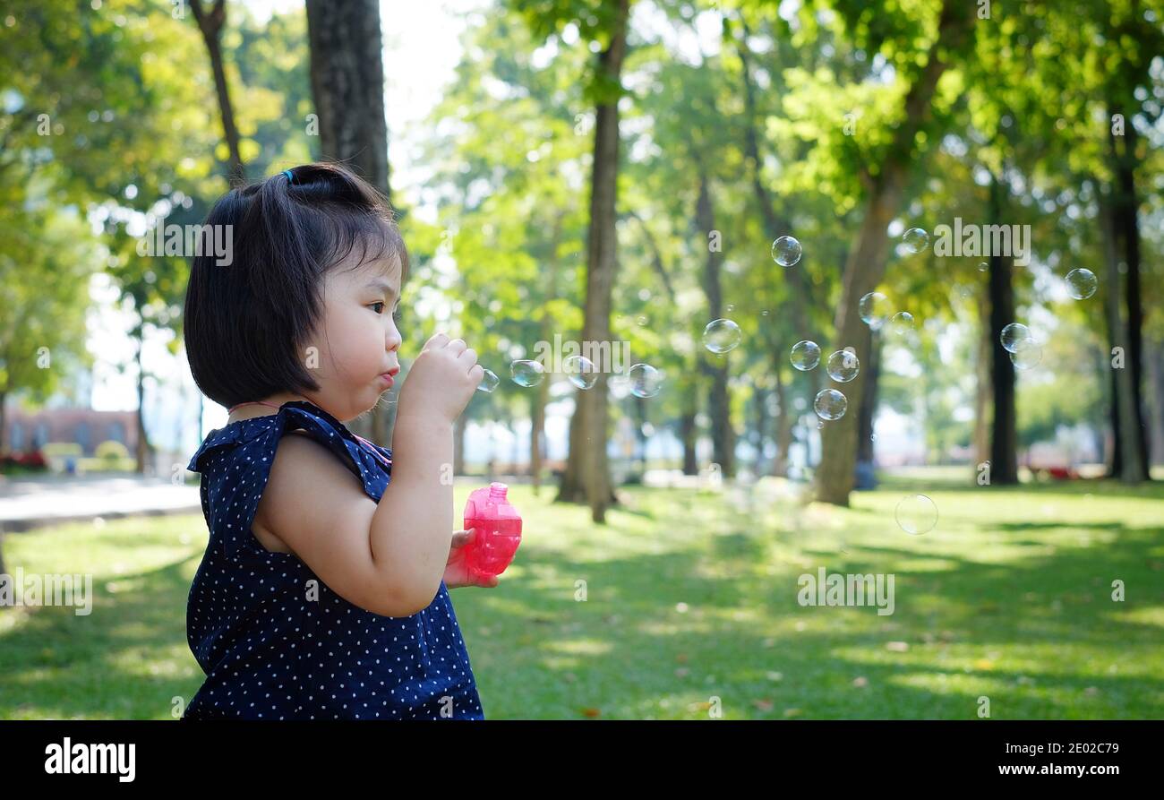 Une jolie fille asiatique jouant au parc avec des bulles savonnables, les soufflant dans l'air. Banque D'Images