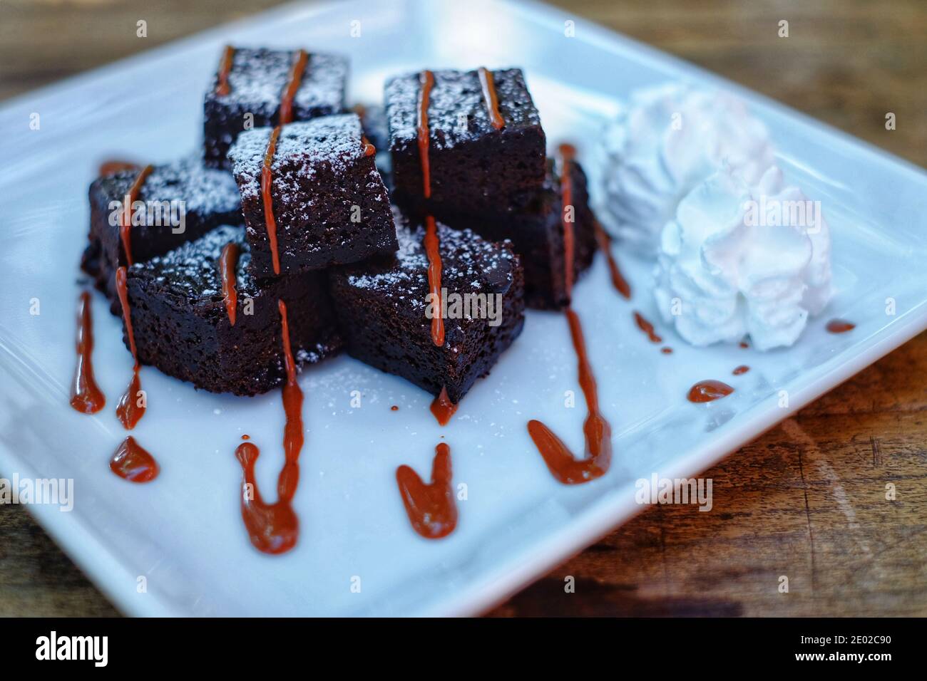 Une portion de brownies avec une source sucrée de goutte de caramel et de crème fouettée blanche servie sur un plat blanc avec de la poudre de sucre. Banque D'Images