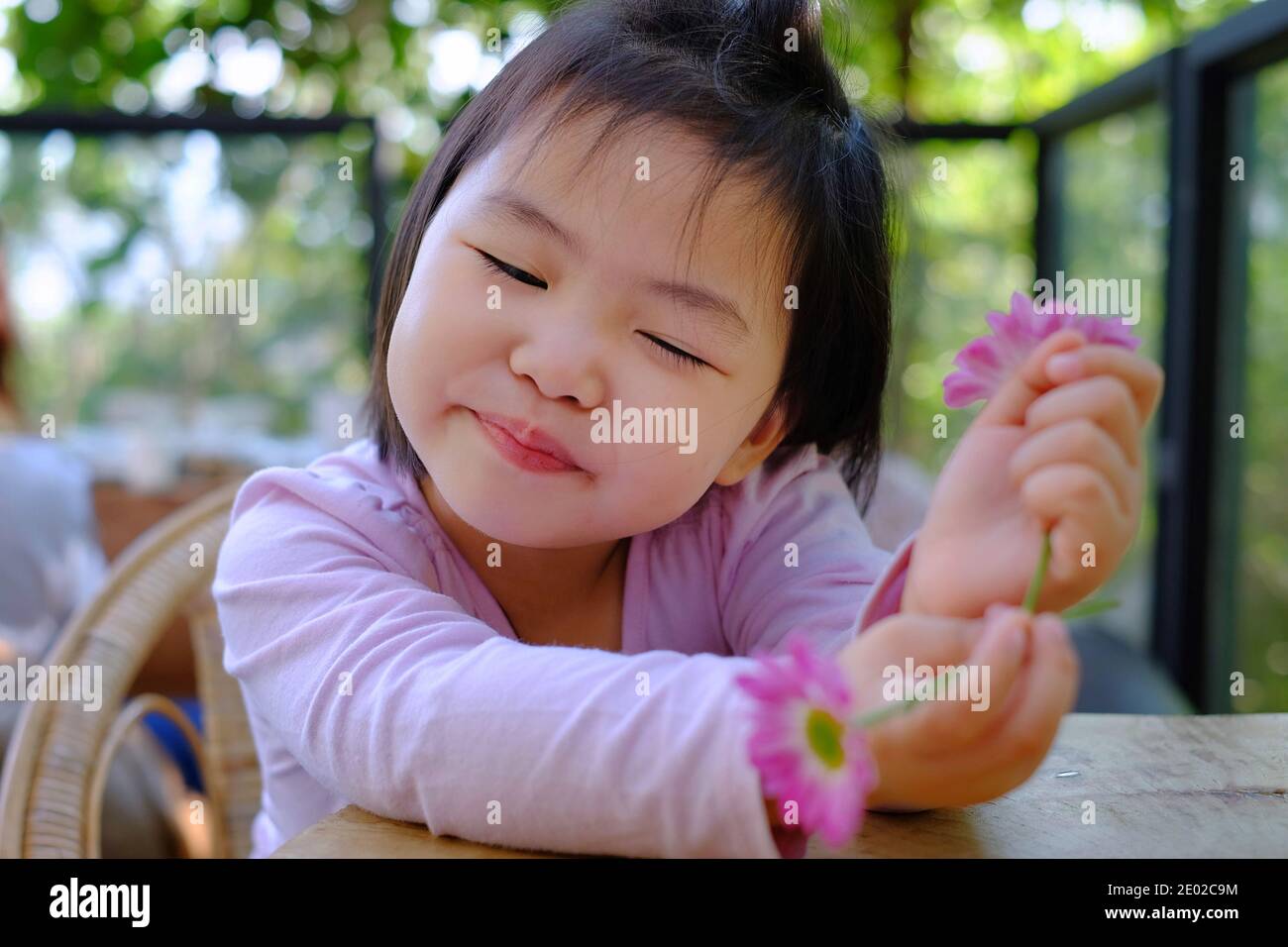 Une jolie petite fille asiatique timide assise près d'une table dans un café, se détendant et apprécier ses jolies fleurs roses, souriant. Banque D'Images