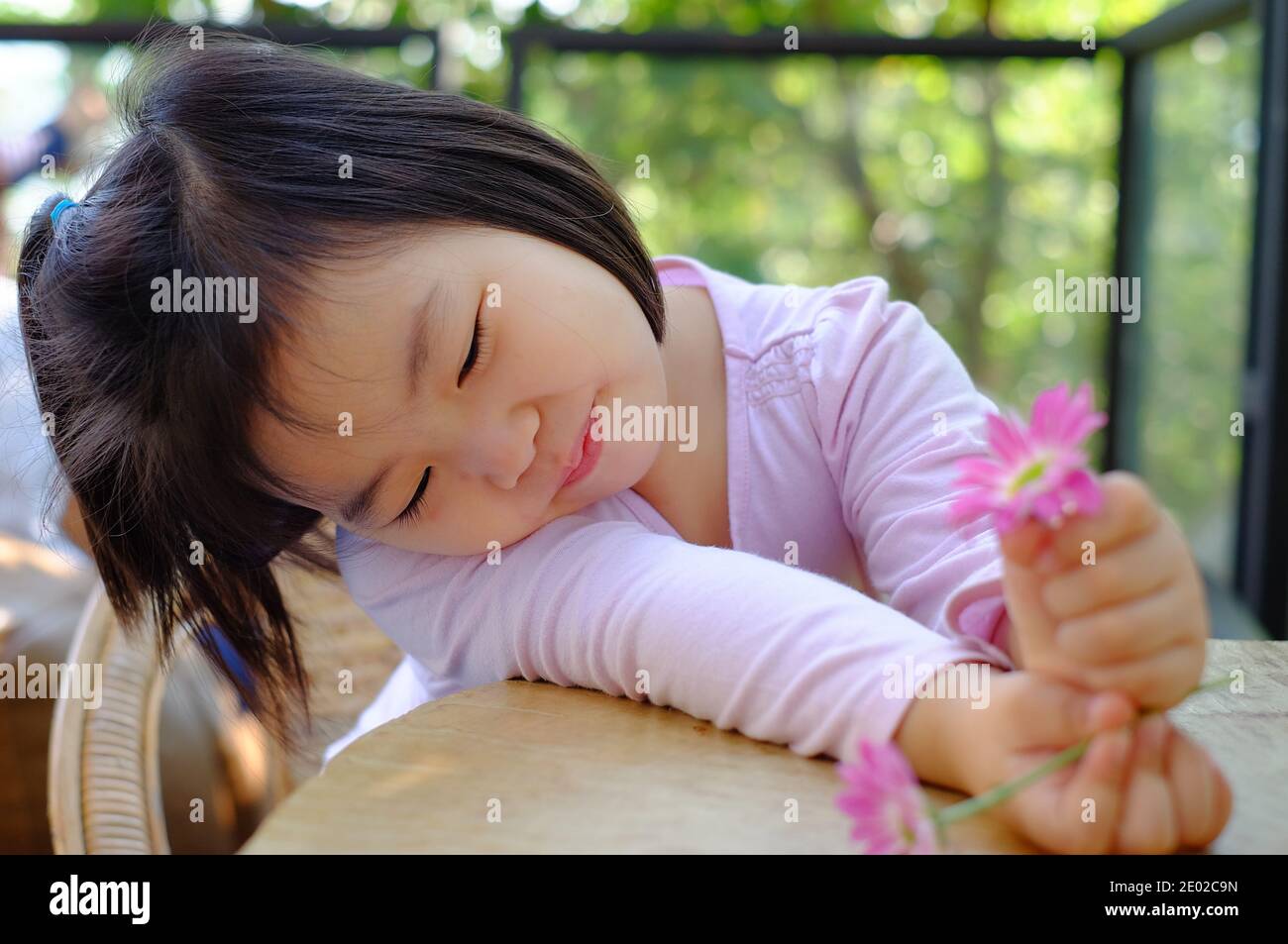 Une jolie petite fille asiatique timide assise près d'une table dans un café, se détendant et apprécier ses jolies fleurs roses, souriant. Banque D'Images