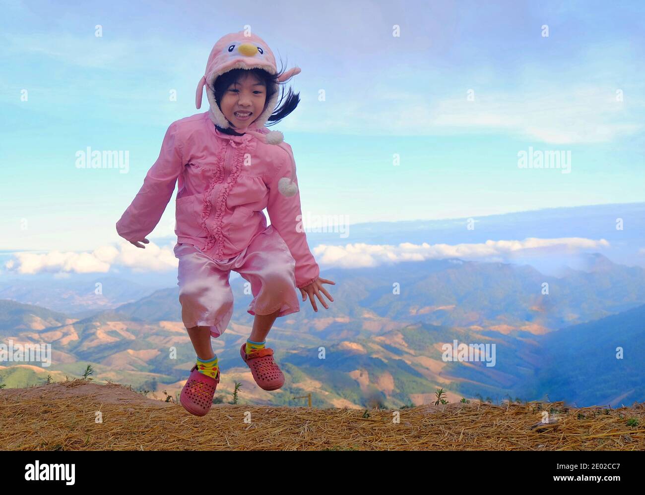 Une jolie fille asiatique sautant pour la joie sur une montagne avec vue sur la montagne et la vallée et ciel bleu vif en arrière-plan. Banque D'Images