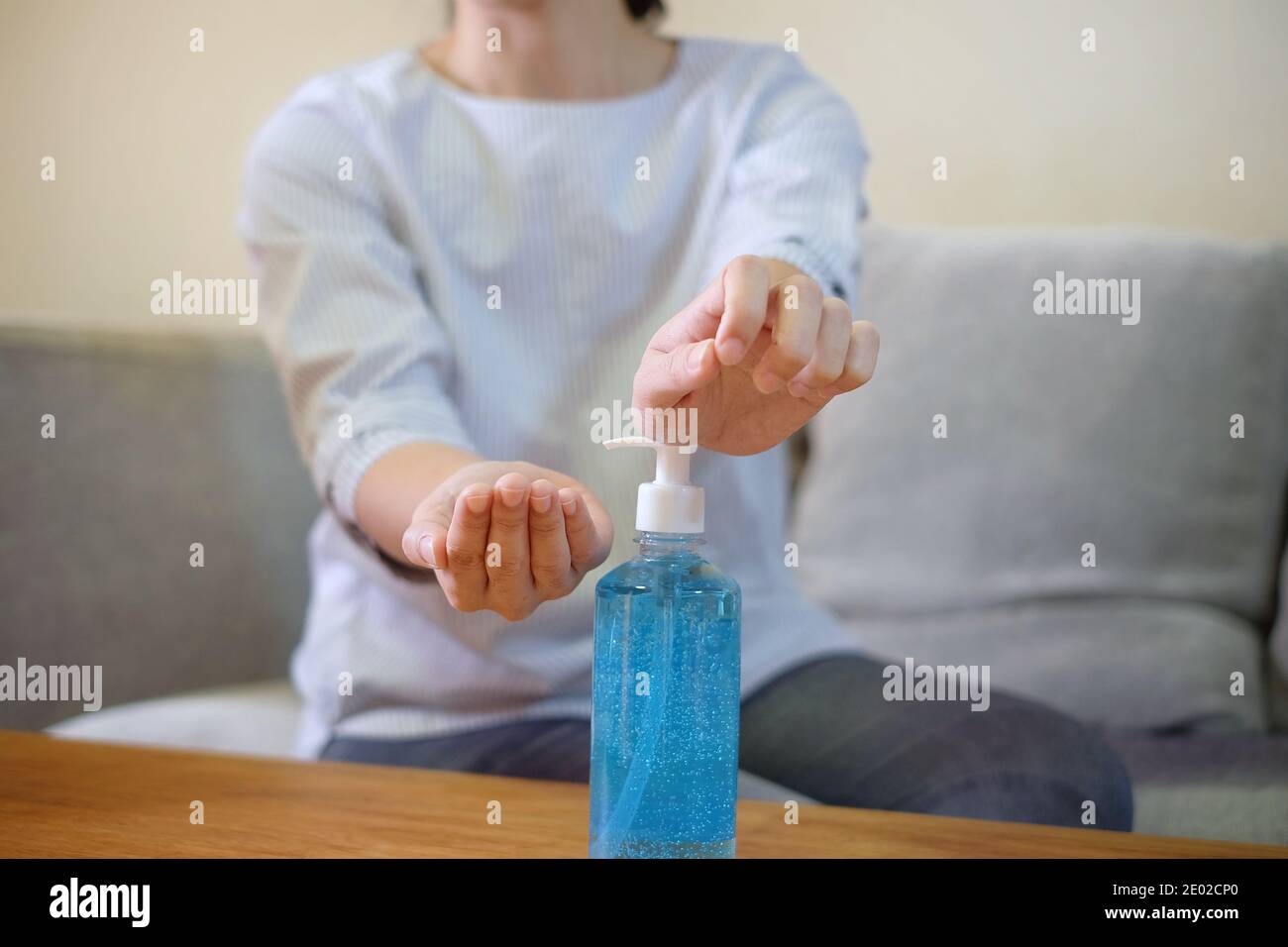 Une femme pressant une bouteille transparente de gel antibactérien bleu sur une table en bois pour nettoyer ses mains. Banque D'Images