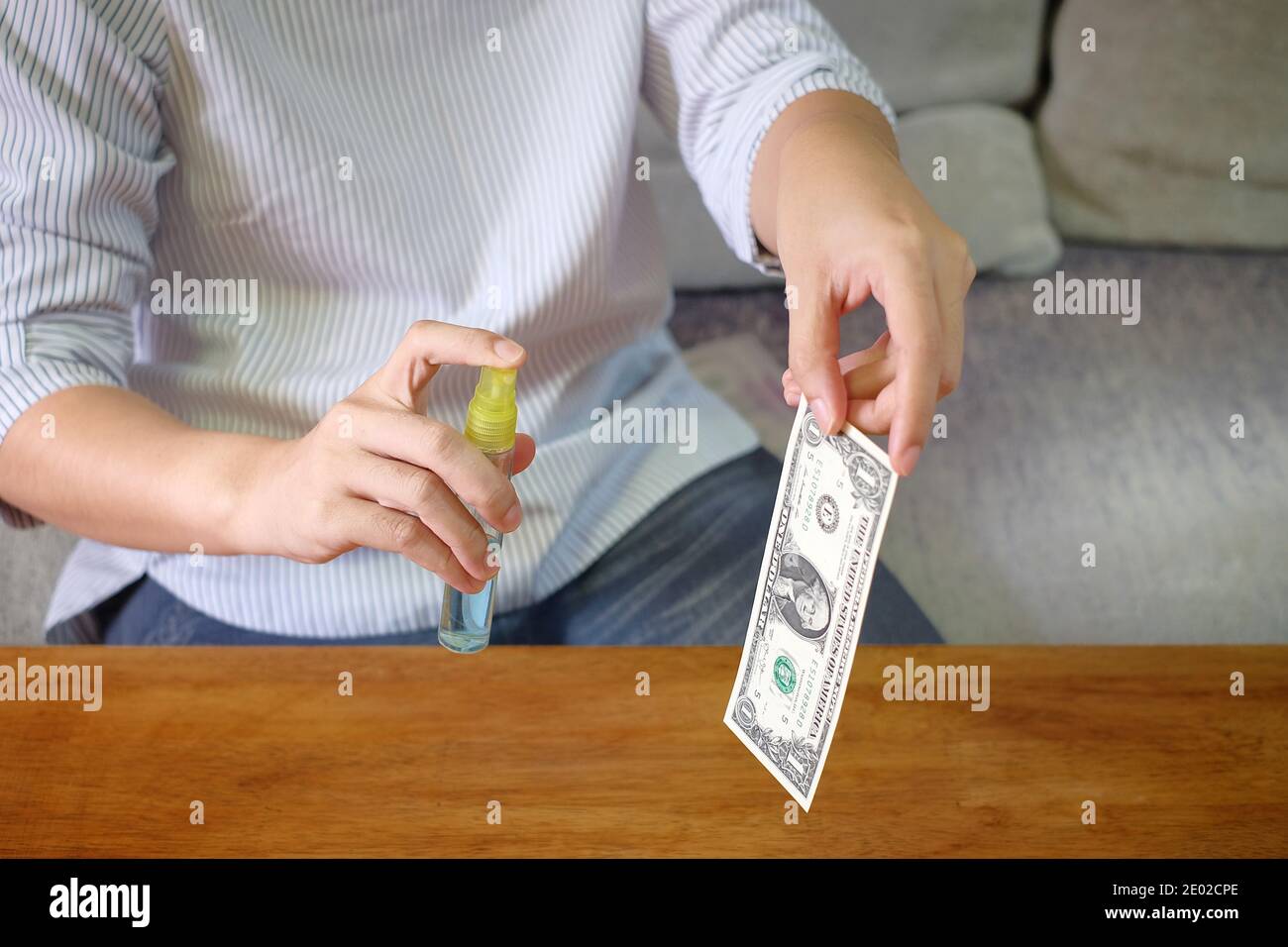Une femme asiatique avec un masque facial désinfecte ses billets de banque aux États-Unis à l'aide d'alcool spray. Banque D'Images