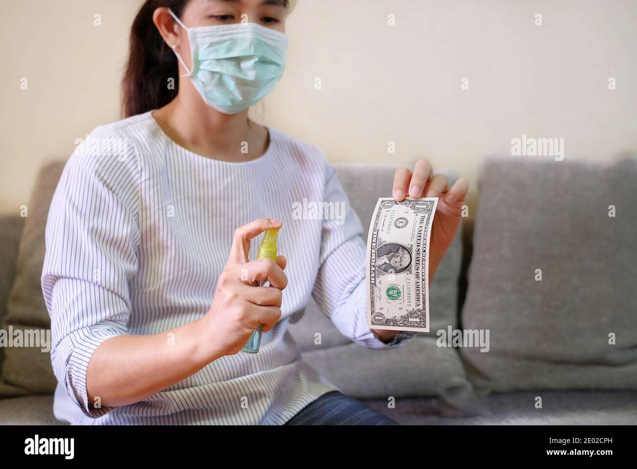 Une femme asiatique avec un masque facial désinfecte ses billets de banque aux États-Unis à l'aide d'alcool spray. Banque D'Images