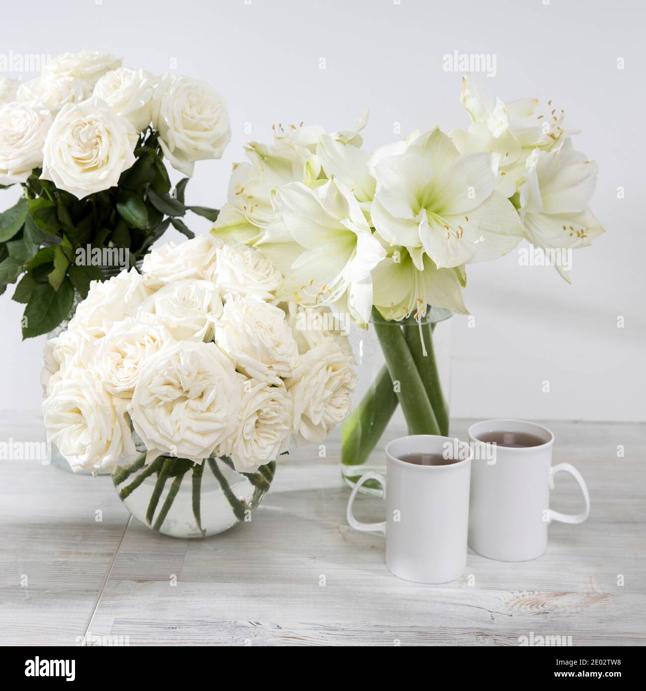 Roses blanches, nénuphars, dans des vases ronds avec deux tasses de café sur la table pour une occasion spéciale comme décoration de cuisine. Copier l'espace Banque D'Images