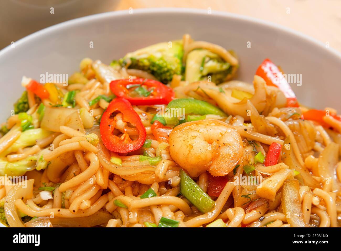 Nouilles de fruits de mer épicées de couleur dorée avec crevettes, brocoli, piment dans une assiette sur une table en bois Banque D'Images