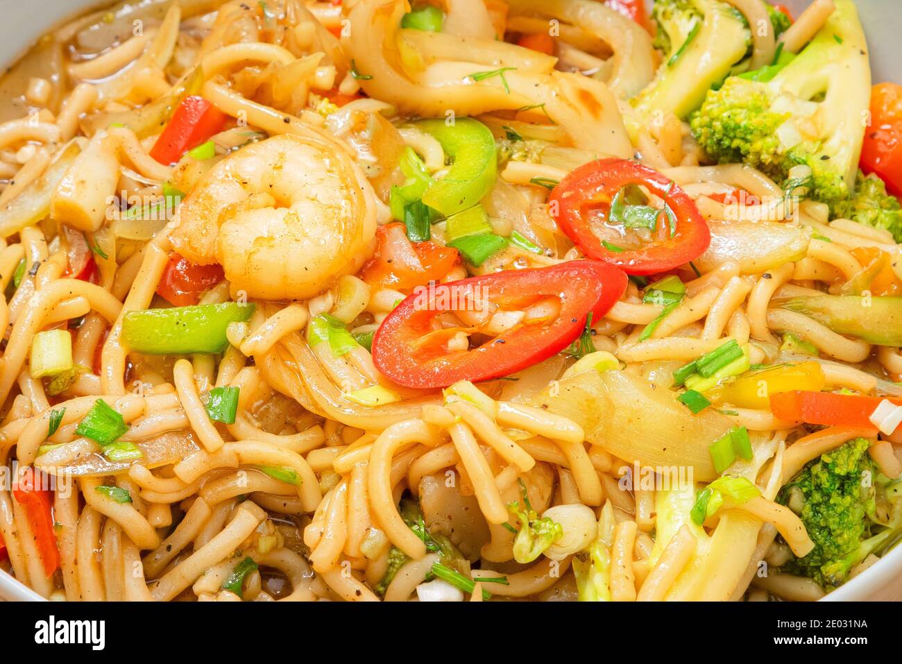 Nouilles de fruits de mer épicées de couleur dorée avec crevettes, brocoli, piment dans une assiette sur une table en bois Banque D'Images
