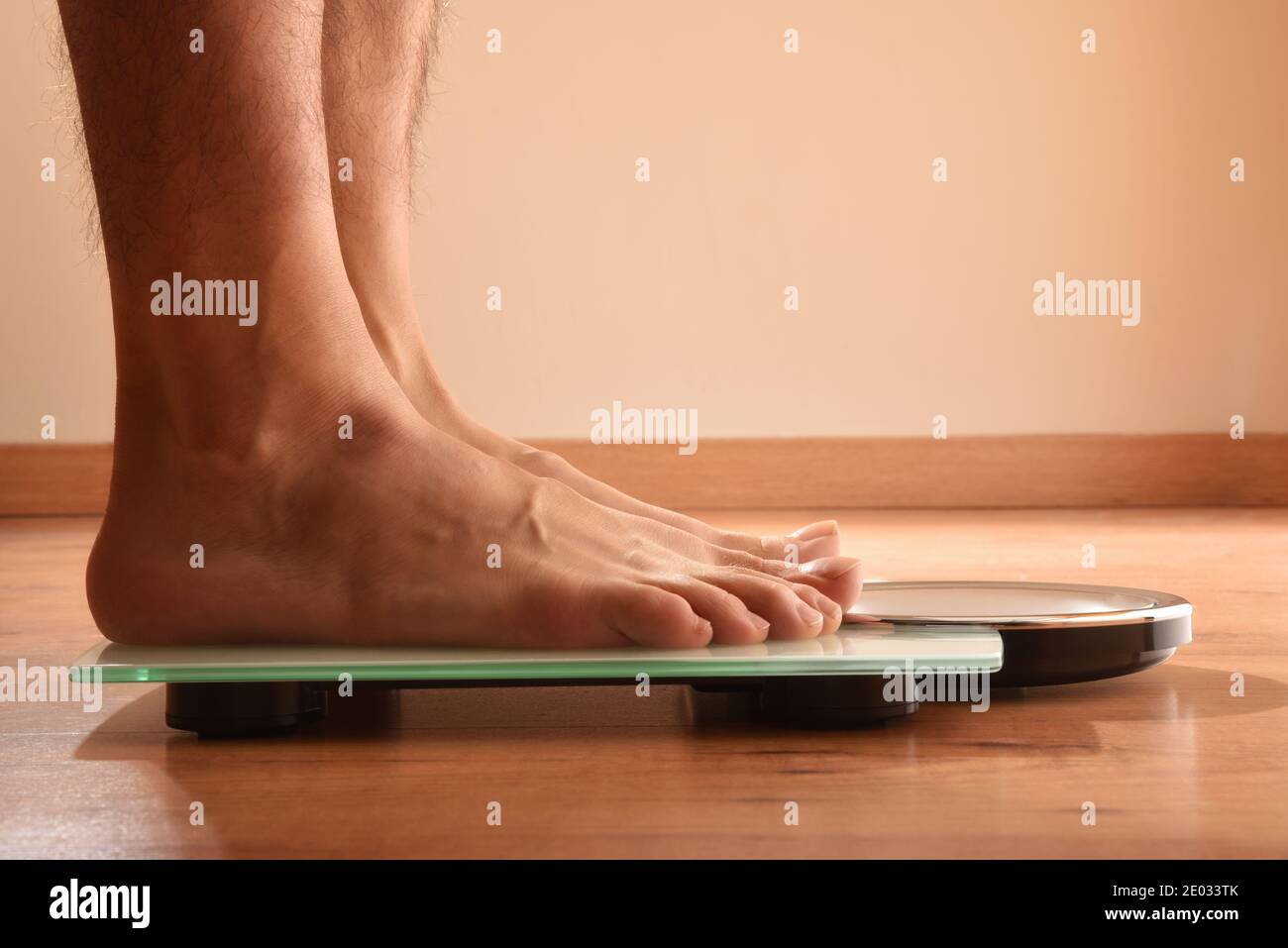 Homme se pesant sur une balance en verre blanc sur un parquet. Vue avant. Composition horizontale. Banque D'Images