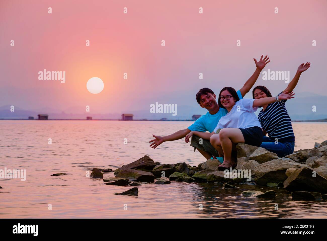 Père de famille asiatique mère et fille adolescente heureux assis dessus le front de mer au lac au soleil d'eau dans le ciel orange magnifique paysage de la nature au soleil Banque D'Images