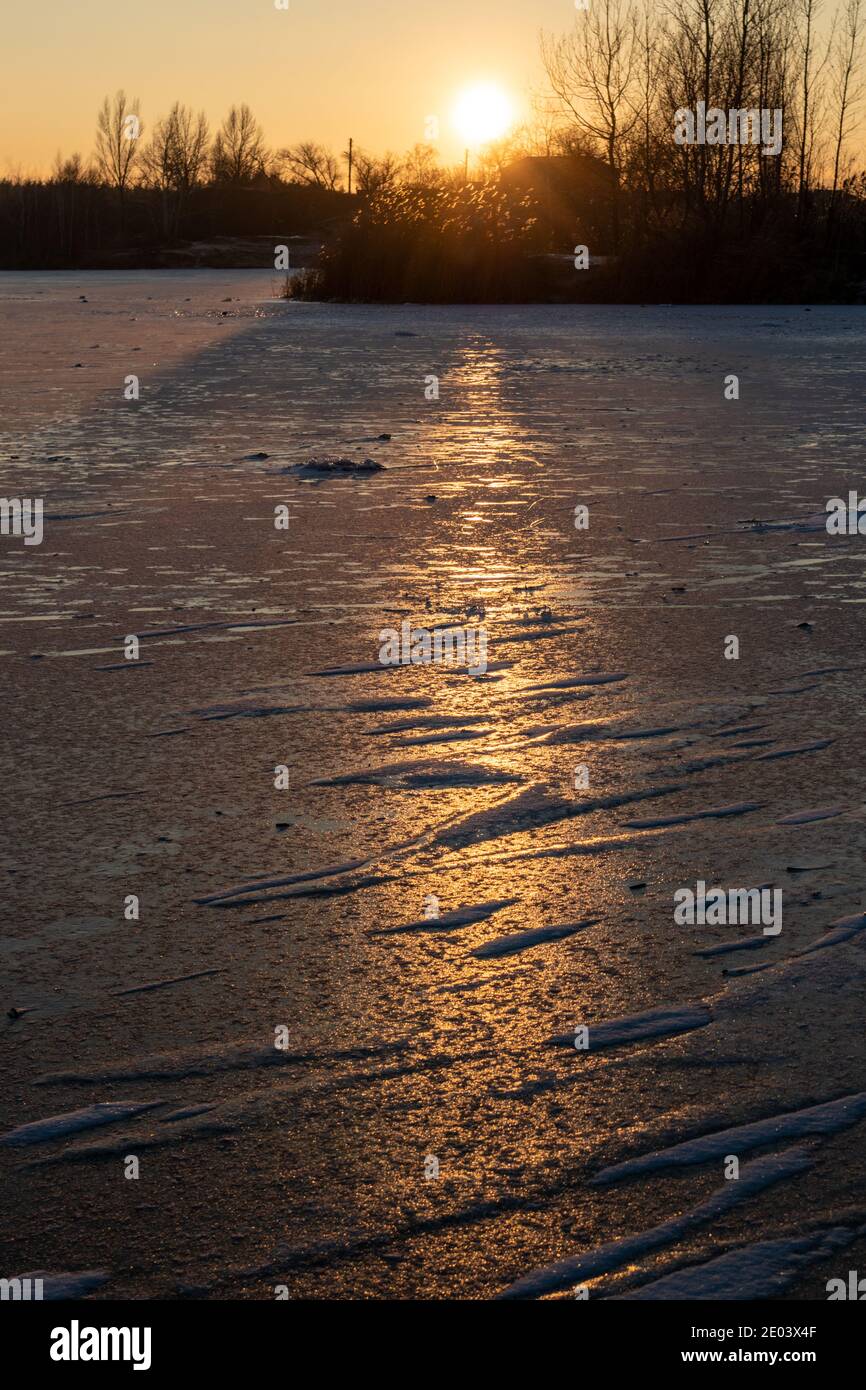 Glace gelée froide surface profonde du lac recouverte de neige en gros plan étincelant sur fond de lumière orangée et chaude au coucher du soleil Banque D'Images