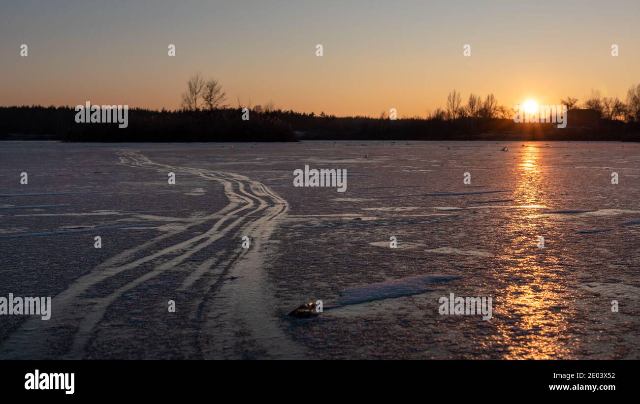 Coucher de soleil orange sur un lac gelé avec des lignes de patinage sur glace sauvage, de longues ombres et un ciel clair Banque D'Images