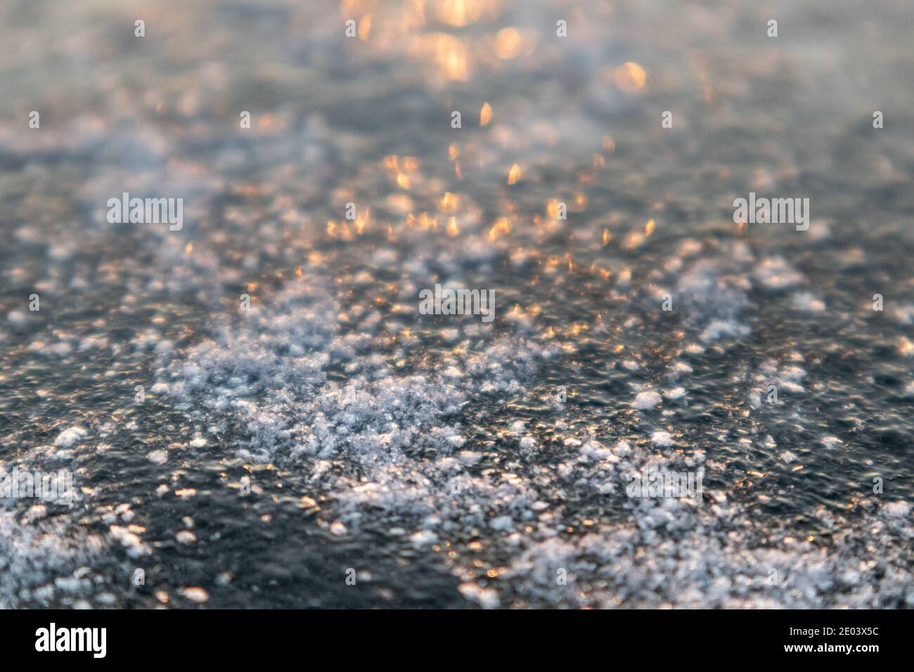 Glace glacée froide profonde surface du lac couverte de neige en gros plan étincelant de lumière orangée. Arrière-plan flou Banque D'Images
