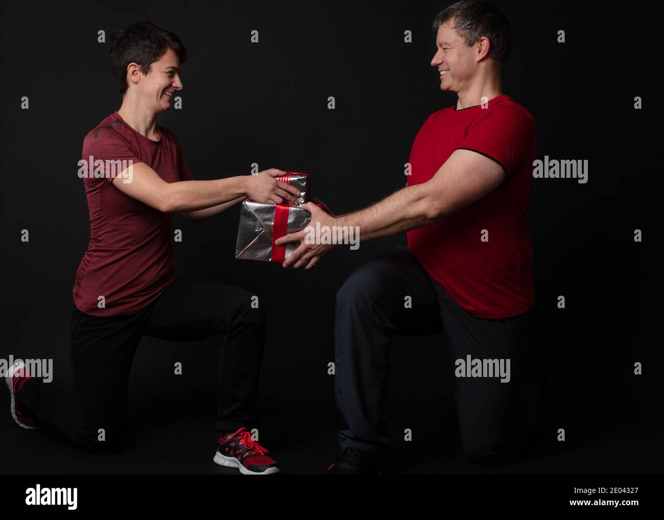Un couple d'entraîneurs personnels qui tient une boîte cadeau enveloppée d'une feuille d'argent et d'un ruban rouge. Banque D'Images