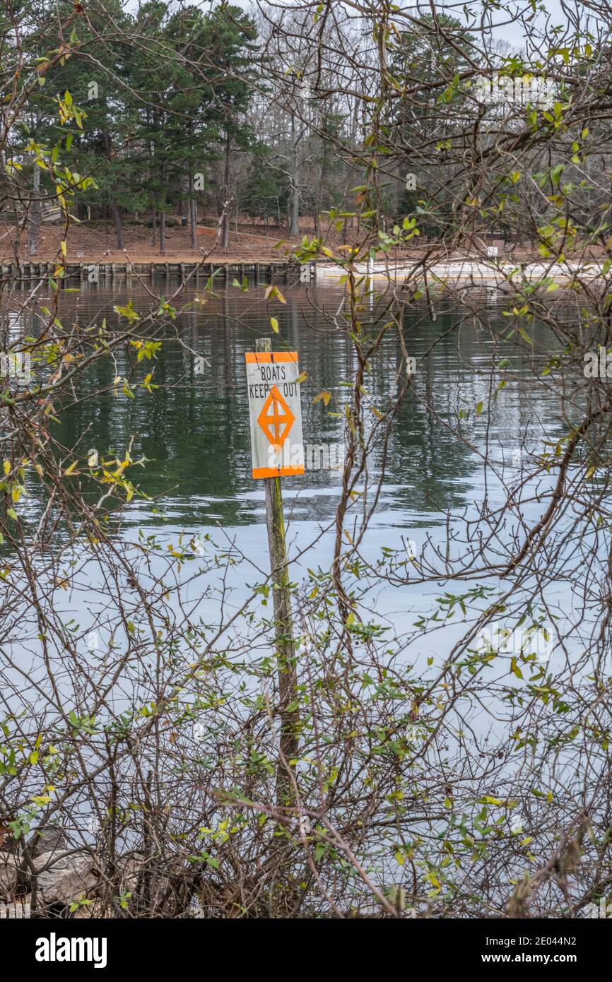 Un panneau orange vif qui indique que les bateaux restent à l'extérieur un symbole nautique sur un ancien poteau dans l'eau par la rive du lac avec le parc avec piscine Banque D'Images