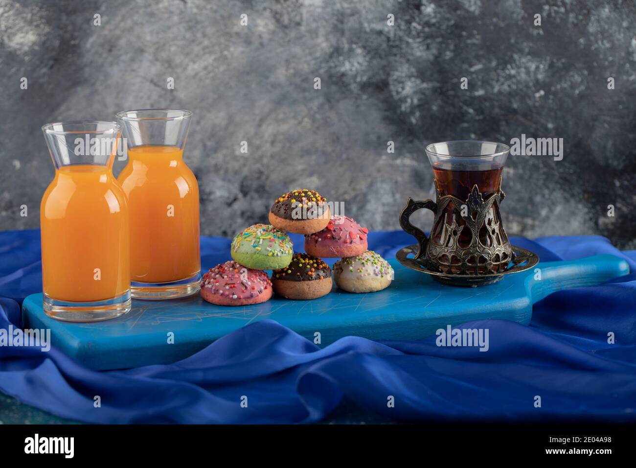 Beignets doux colorés avec des pots de jus en verre et un tasse de thé Banque D'Images