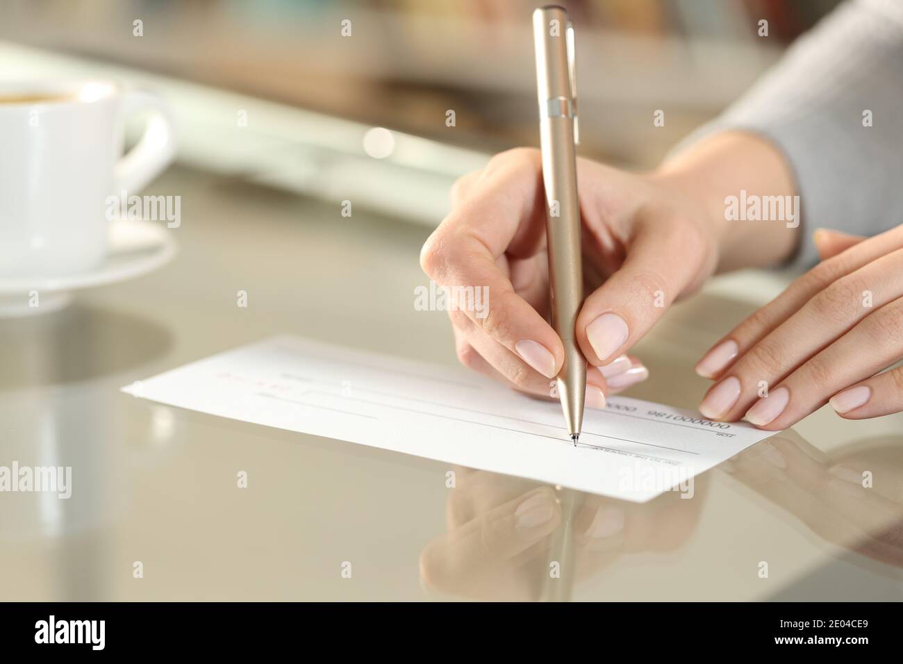 Gros plan d'une main de femme écrivant le chèque de banque à effectuer un paiement sur une table Banque D'Images