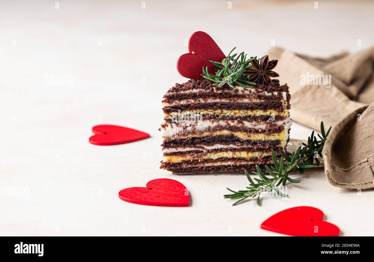 Le morceau de gâteau enrobé de chocolat et les coeurs rouges sur fond de béton clair. Décor festif de la Saint-Valentin. Gâteau au miel russe, Medovik. Sélectif Banque D'Images