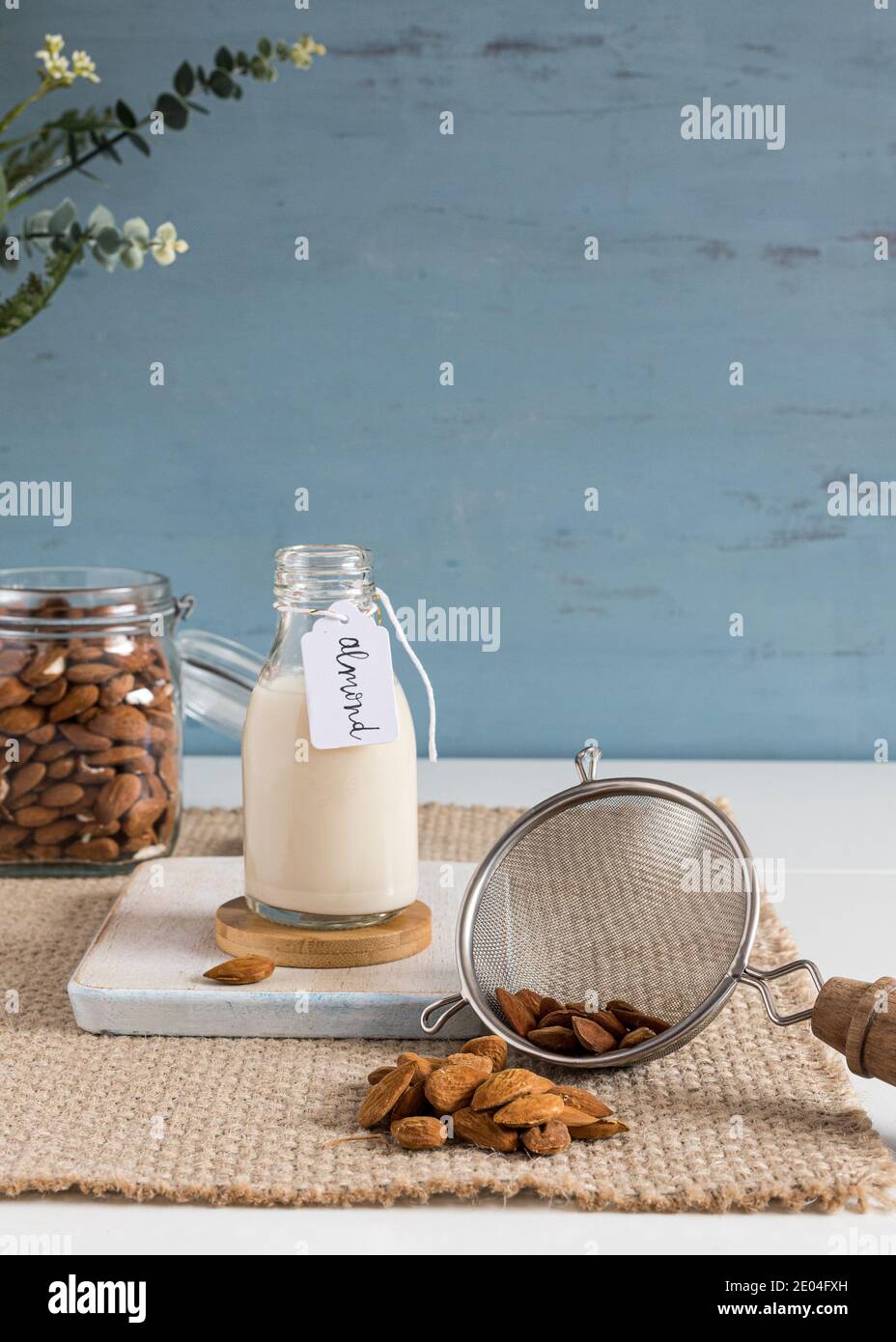 Lait d'amande dans une bouteille à côté d'un pot et d'une passoire pleine d'amandes. Vue verticale. Banque D'Images