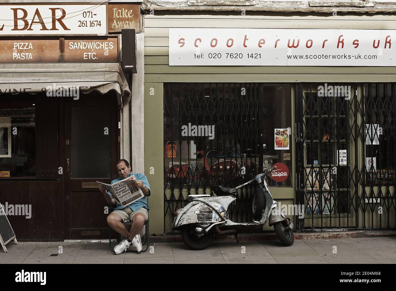 GRANDE-BRETAGNE / Londres /Man est en train de lire son journal devant un magasin de scooter d'époque et à côté de lui un Vespa . Banque D'Images