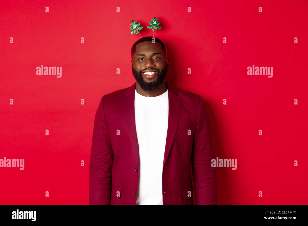 Joyeux Noël. Joyeux homme afro-américain qui célèbre le nouvel an, portant  un bandeau amusant et souriant, debout sur fond rouge Photo Stock - Alamy
