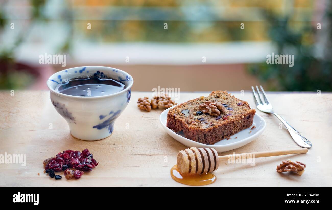 Une tranche de gâteau végétalien avec de super fruits et des noix, du miel et une tasse de thé sur une table en bois Banque D'Images
