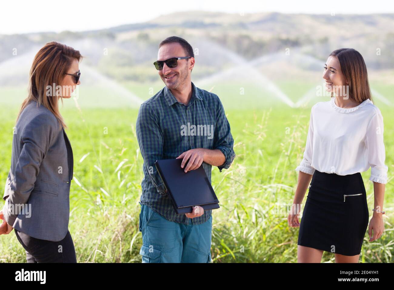 Gens d'affaires dans un champ vert avec système d'irrigation agricole. Arroseurs d'eau en arrière-plan. Banque D'Images