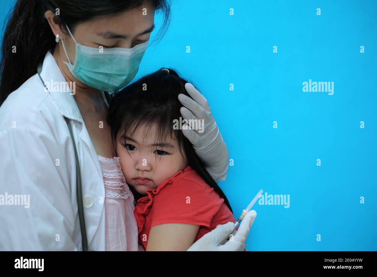 Une jolie jeune fille asiatique se sentant effrayée et nerveuse avant se faire vacciner est réconforté par son médecin qui l'est port d'un masque chirurgical avec un coup Banque D'Images