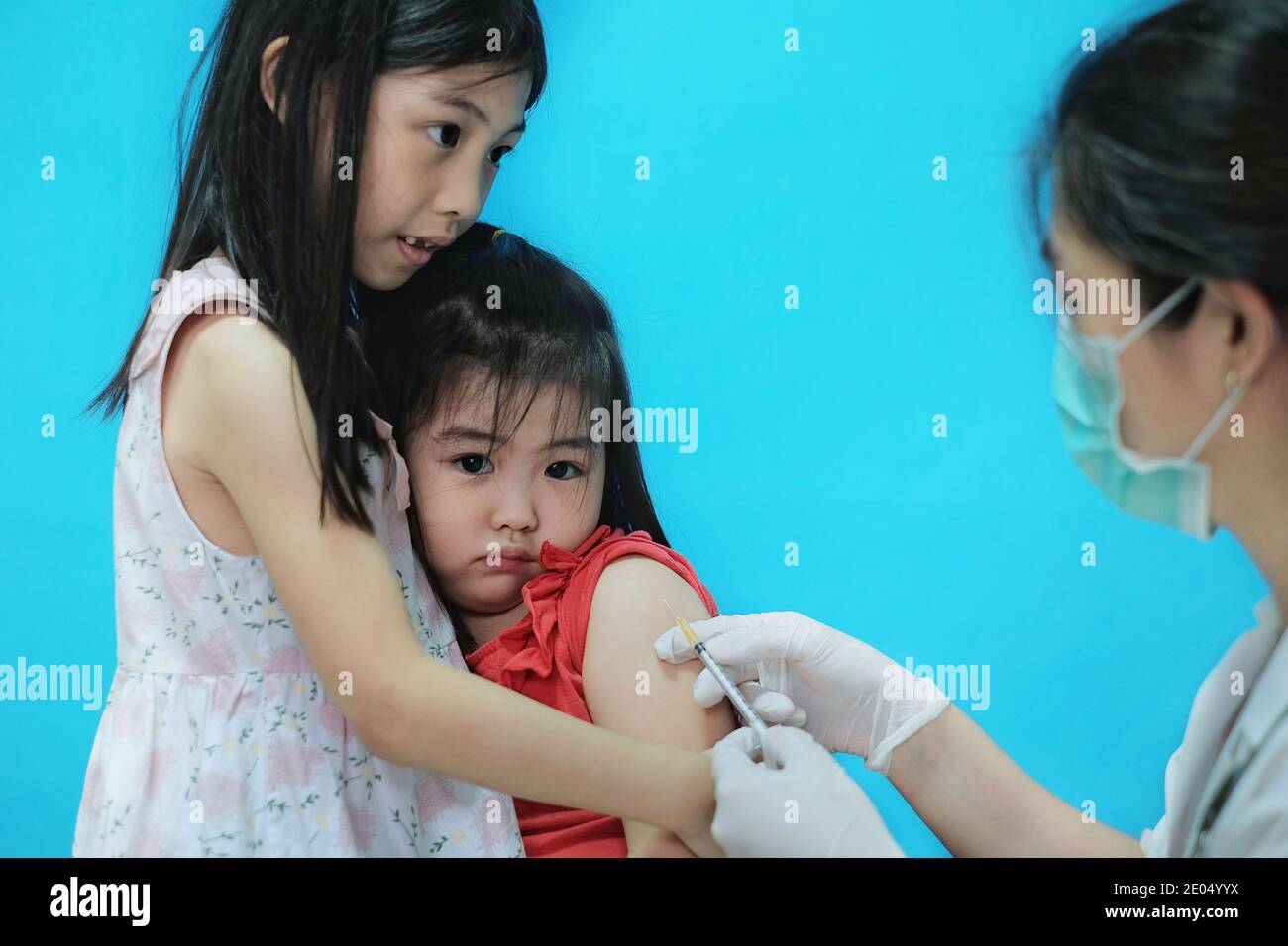 Une jolie jeune fille asiatique se sentant effrayée et nerveuse avant se faire vacciner par son médecin qui porte une chirurgie masque avec des gants en caoutchouc blanc est Banque D'Images