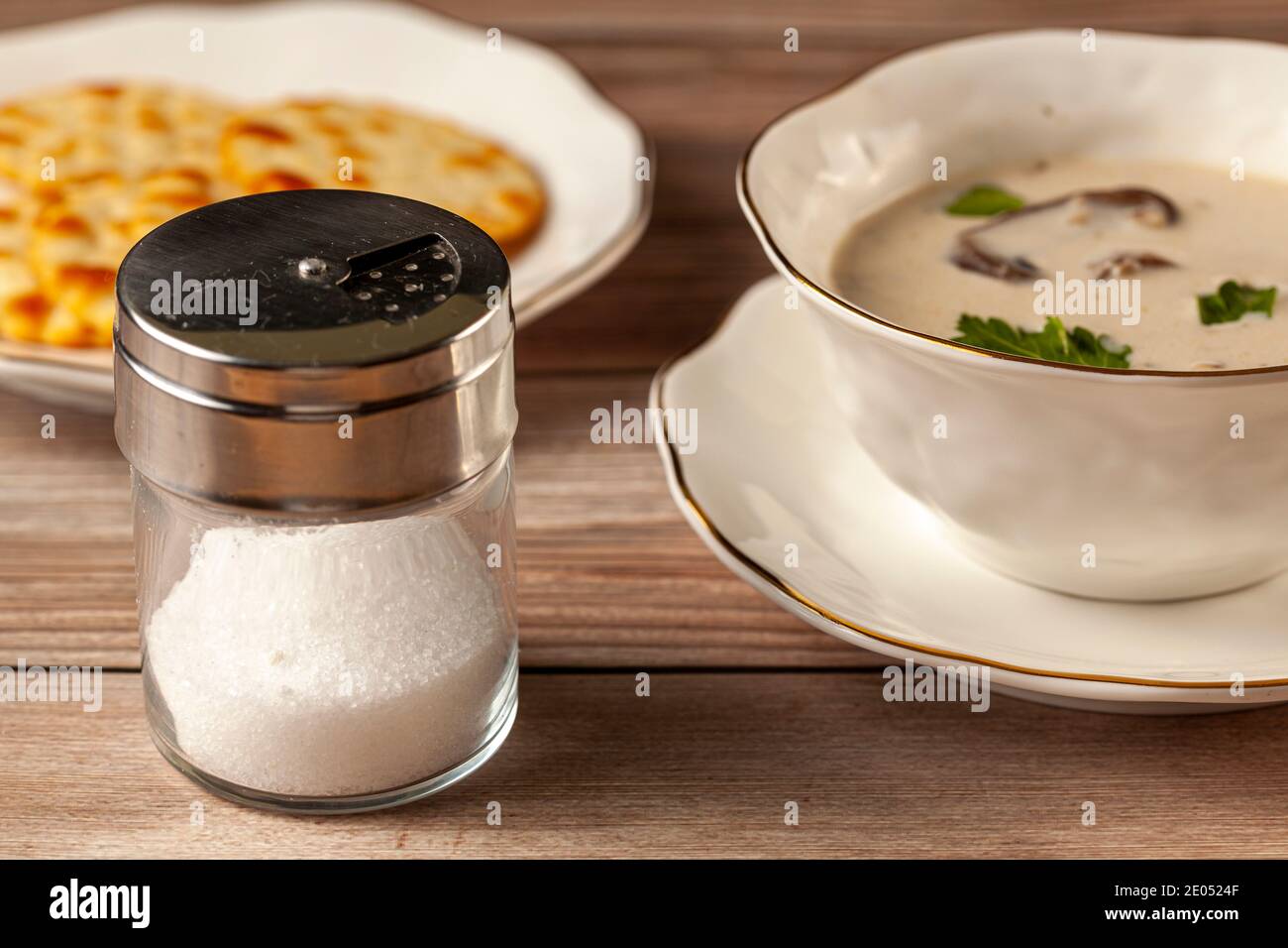 Un saupoudreur en verre avec une tasse de soupe crémeuse aux champignons et des craquelins salés à l'arrière-plan. Une image pour la consommation de sel coeur et hypertens Banque D'Images