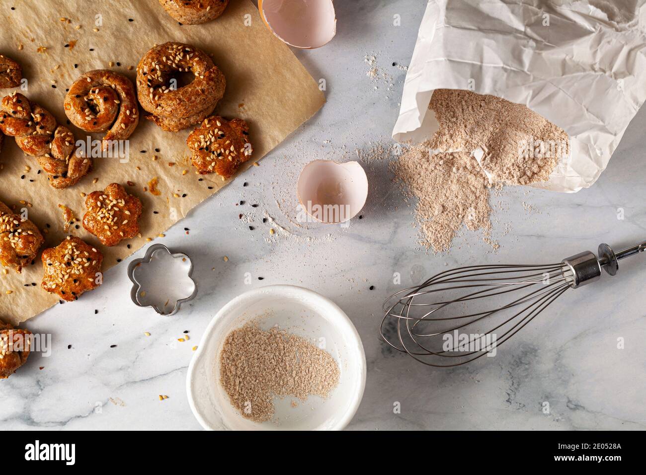 Image plate de pâte fraîche faite à la main sur du papier de cuisson avec des graines éparpillées sur un comptoir de cuisine en marbre. Un fouet, des coquilles d'œufs, de la farine de blé entier Banque D'Images