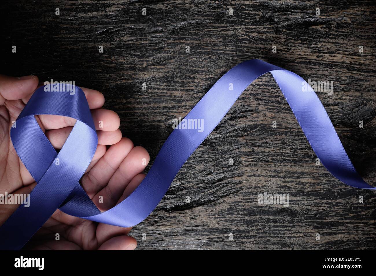 Vue de dessus du ruban bleu periwinkle tenu à la main d'un homme sur fond de bois avec espace de copie. Sensibilisation au cancer de l'estomac et de l'œsophage, troubles de l'alimentation Banque D'Images
