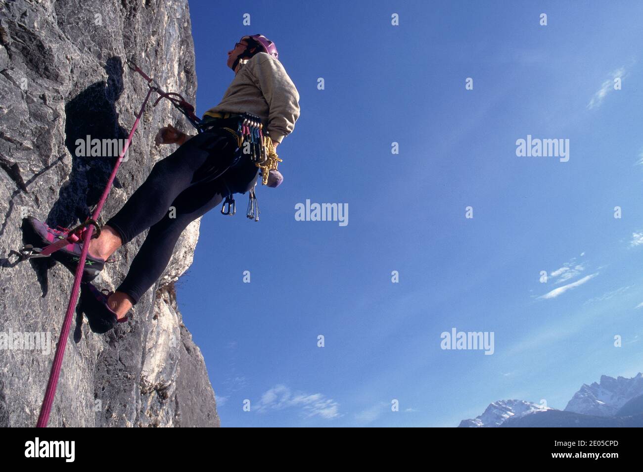 Grimpeur mâle caucasien grimpant sur un mur escarpé. En arrière-plan un paysage alpin d'été. Ciel clair, lumière du jour. Alpes italiennes, Europe. Banque D'Images