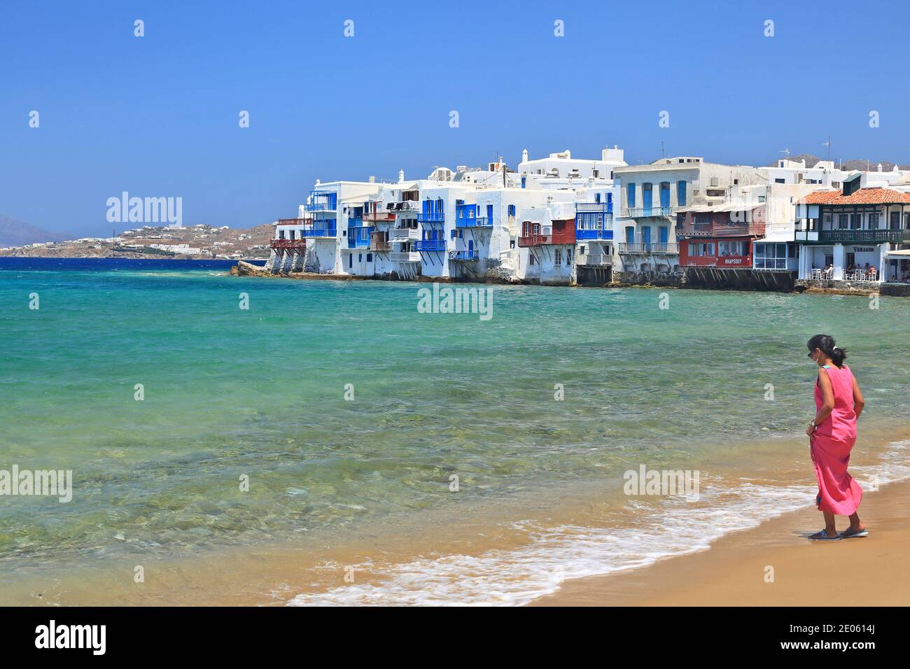 L'île de Mykonos, une femme en robe rose, a le goût de la température de la mer, sur la plage de sable de Chora, dans les îles Cyclades, en Grèce, en Europe Banque D'Images