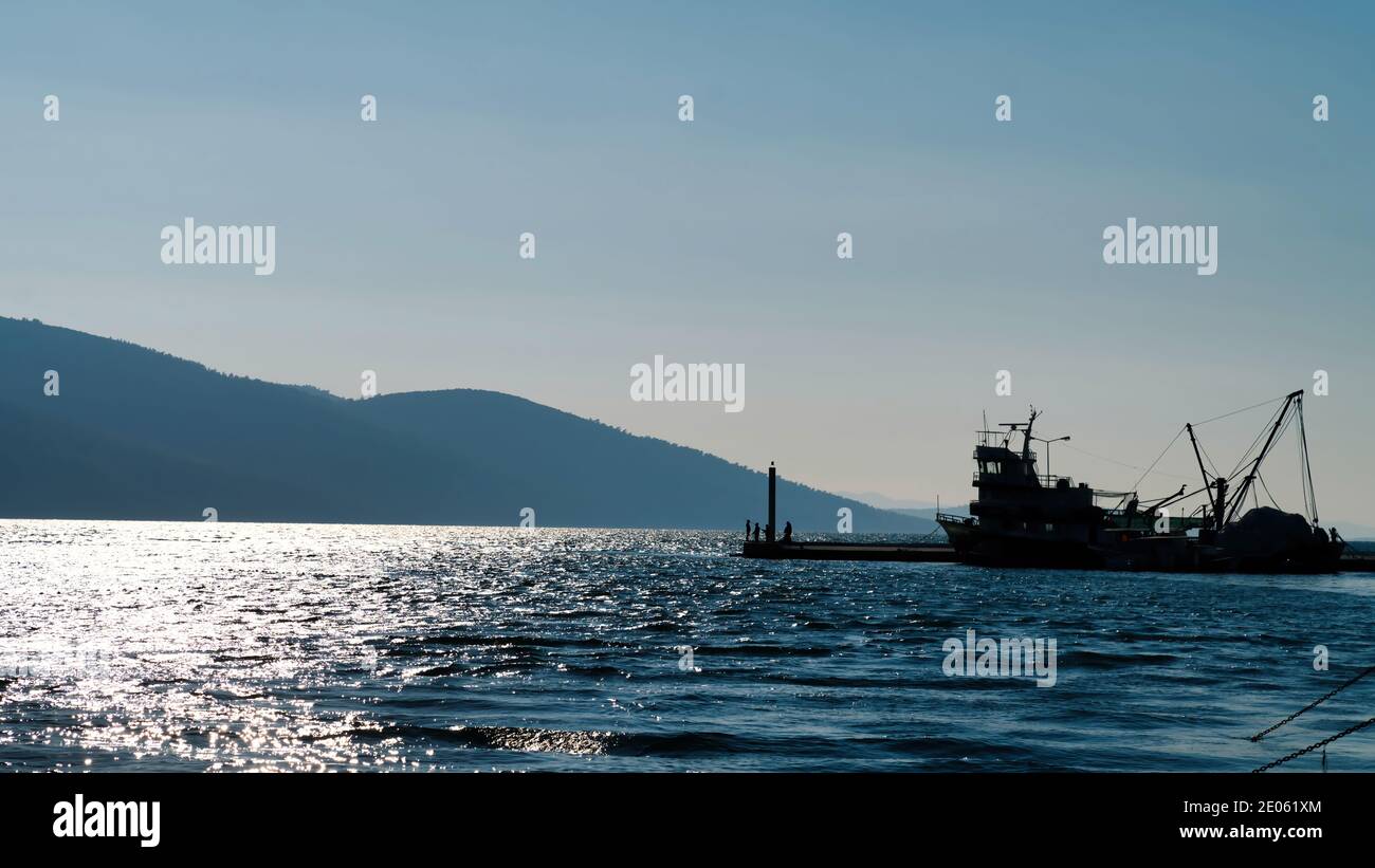 Marmaris, Akyaka, Turquie - novembre 2020 : silhouette d'un bateau de pêche avec des personnes non identifiées et d'un phare dans le port du village d'Akyaka Banque D'Images