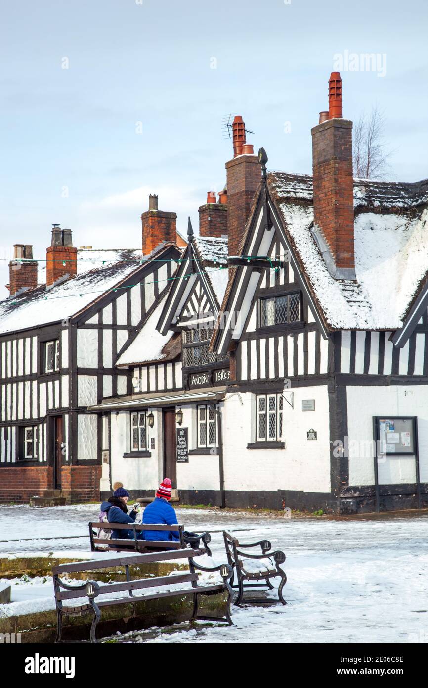 Personnes assises sur un banc sur la place du marché enneigée À Sandbach à Cheshire en hiver en noir et white half timbered coaching inn Banque D'Images