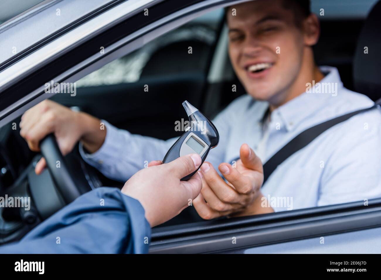 policier donnant un alcootest à l'homme ivre et gai assis en voiture sur un fond flou Banque D'Images