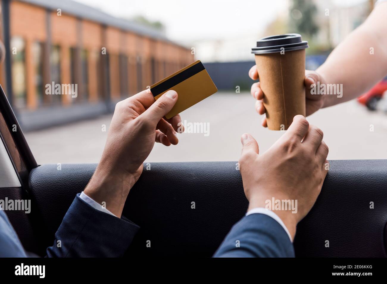 Vue rognée d'un homme d'affaires tenant une carte de crédit et prenant un café pour aller du vendeur près de la voiture Banque D'Images