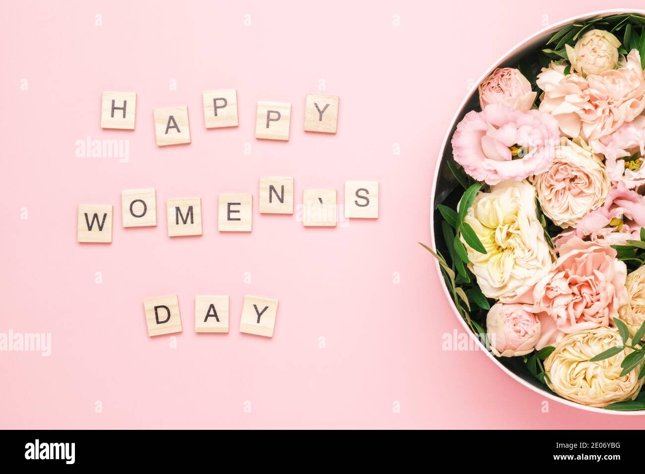 Happy Women Day lettering sur les carrés en bois avec des lettres sur le fond rose et une grande boîte ronde avec des fleurs rouges et des roses. Banque D'Images