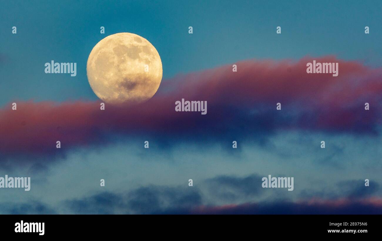 Pleine lune qui s'élève au-dessus des nuages roses dans le ciel bleu Banque D'Images