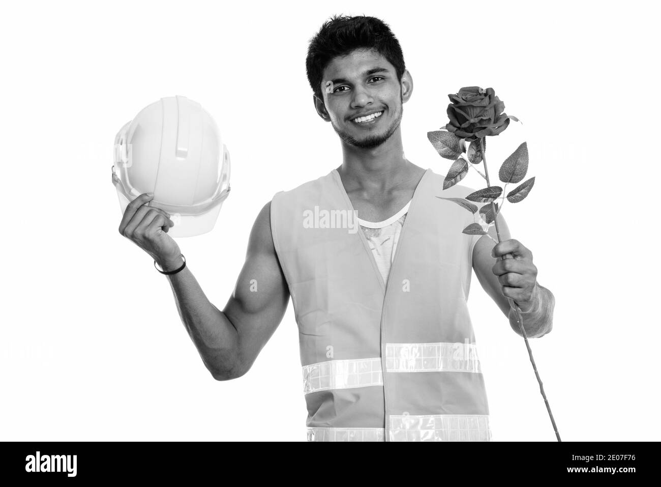 Young happy Indian man construction worker smiling while holding casque de sécurité et donner rose rouge prêt pour la Saint-Valentin Banque D'Images