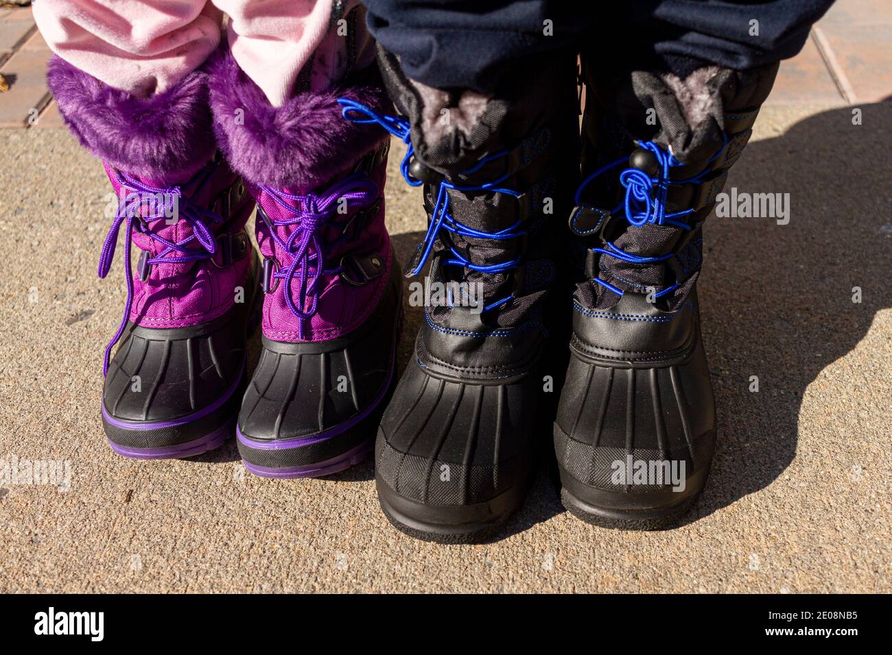 Taille vers le bas gros plan image d'un garçon et d'une fille sont debout côte à côte sur le béton. Ils portent des bottes d'hiver et des pantalons de survêtement imperméables et épais. Un confluage Banque D'Images